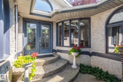 Double entry doors with decorative glass inserts, exposed aggregate steps, arched window with dark trim, bay window with dark trim, and a prominent skylight - 