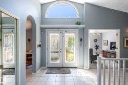 Vaulted entry featuring a decorative arched window, double doors with frosted glass inserts, and white tile flooring - 