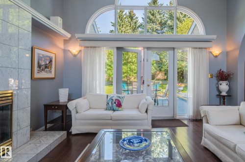 Arch-top window with transoms, double glass-paneled doors, wood-finish flooring, tiled fireplace surround, and recessed wall sconces - 8 Edgemont Point(E), St. Albert, AB 
