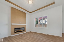 Recessed ceiling details with accent trim, built-in electric fireplace with mantel, window with white trim, wood-finish flooring, and a decorative ceiling light fixture - 
