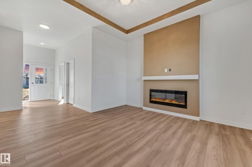 Wood-finish flooring throughout, recessed ceiling lighting, a built-in electric fireplace with a white mantel, and a decorative tray ceiling detail - 32 Dalquist Bay, Leduc, AB 