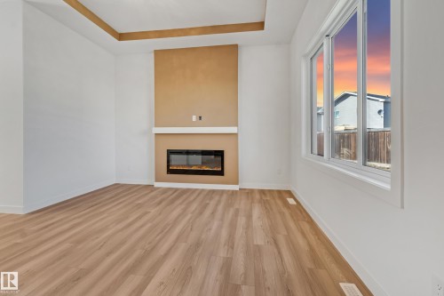 Recessed ceiling with accent paint, wood-finish flooring, electric fireplace with mantel, and large windows - 32 Dalquist Bay, Leduc, AB 
