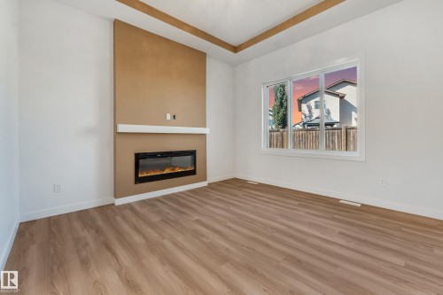 Wood-finish flooring, recessed ceiling detail, electric fireplace, large window, and clean white walls - 32 Dalquist Bay, Leduc, AB 