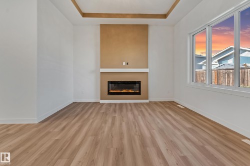 Wood-finish flooring, accent wall with electric fireplace, white mantel, and large window - 32 Dalquist Bay, Leduc, AB 