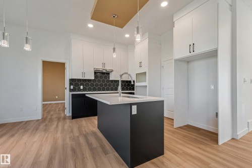 Spacious kitchen featuring an island with an undermount sink, two-tone cabinetry with black hardware, hexagonal tile backsplash, and light wood-finish flooring - 32 Dalquist Bay, Leduc, AB 