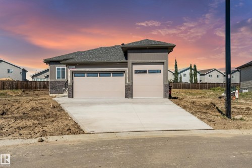 Modern exterior with gray siding and stone accents, featuring a two-car garage with contemporary doors, and a single-car garage with a matching door - 32 Dalquist Bay, Leduc, AB 