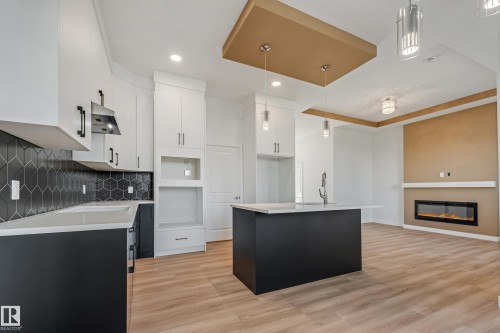 Open-concept kitchen with wood-finish flooring, a central island featuring an integrated sink, a built-in fireplace, and a striking coffered ceiling - 32 Dalquist Bay, Leduc, AB 