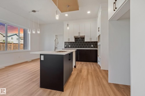 Open-concept kitchen and dining area featuring wood-finish flooring, a kitchen island with an undermount sink, pendant lighting, and a dark hexagonal tile backsplash - 32 Dalquist Bay, Leduc, AB 
