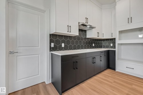 Two-tone cabinetry with matte black hardware, hexagonal tile backsplash, light-toned countertops, stainless steel range hood, and wood-finish flooring - 32 Dalquist Bay, Leduc, AB 