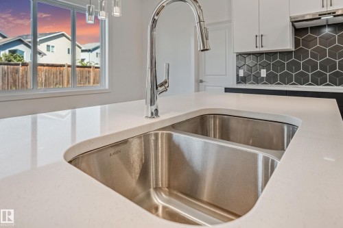 Double basin stainless steel undermount sink, gooseneck pull-down faucet, white solid surface countertop, black geometric tile backsplash, and white shaker-style cabinetry - 32 Dalquist Bay, Leduc, AB 