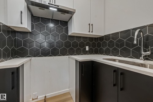 Black geometric tile backsplash, stainless steel sink, chrome faucet, white upper cabinetry, and black lower cabinetry - 32 Dalquist Bay, Leduc, AB 