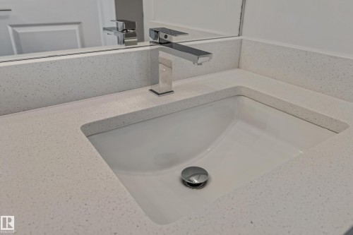 Integrated rectangular sink with polished chrome faucet and speckled light-toned countertop - 32 Dalquist Bay, Leduc, AB 