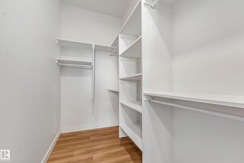 Walk-in closet featuring built-in shelving, multiple hanging rods, and wood-finish flooring - 32 Dalquist Bay, Leduc, AB 
