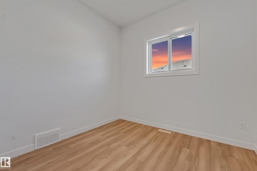 Expansive interior with light wood-finish flooring, white walls, and a window featuring a white frame and trim - 32 Dalquist Bay, Leduc, AB 