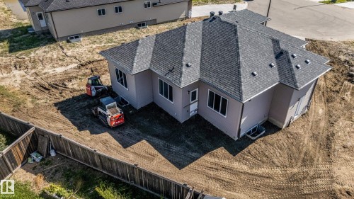 Newly constructed residence featuring a gray shingle roof, light-colored siding, multiple windows, and a partially fenced perimeter - 32 Dalquist Bay, Leduc, AB 
