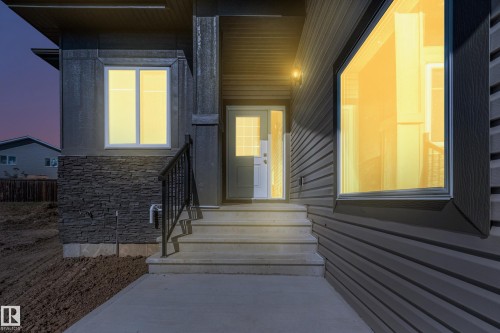 Contemporary exterior featuring horizontal siding, a stone veneer accent, large windows, an exterior light fixture, and a front entry door with a clear glass insert - 32 Dalquist Bay, Leduc, AB 