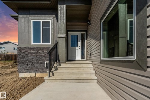 Multi-textured exterior with stone veneer accents, durable siding, and a prominent concrete entryway with steps - 32 Dalquist Bay, Leduc, AB 