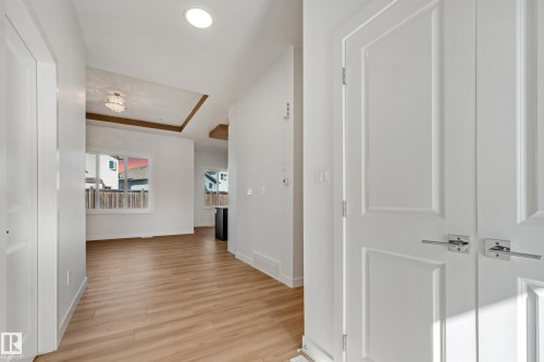 Light wood-finish flooring throughout, white interior doors with polished chrome hardware, recessed lighting, and a tray ceiling with a decorative light fixture - 32 Dalquist Bay, Leduc, AB 
