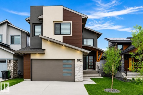 Contemporary exterior featuring multiple facade materials, an integrated garage, a covered entry with wood accents, and tiered front landscaping - 162 Edgewater Circle, Leduc, AB 