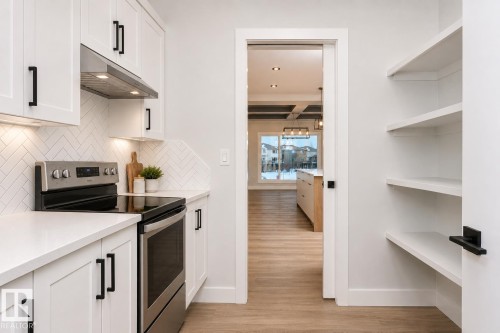 White cabinetry with matte black hardware, stainless steel range, herringbone tile backsplash, integrated under-cabinet lighting, and open shelving - 162 Edgewater Circle, Leduc, AB 