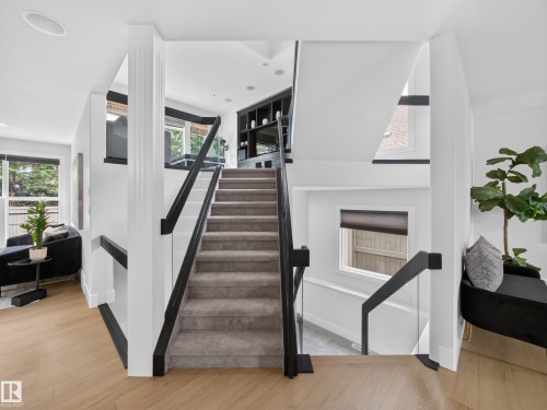Multilevel staircase with carpeted treads and glass panel railings - #59 10550 Ellerslie Rd Sw, Edmonton, AB - Indoor Photo Showing Other Room