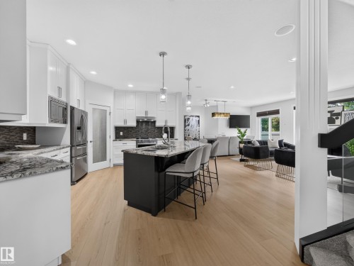 Open-concept kitchen featuring an island with seating, stainless steel appliances, pendant lighting, light wood-finish flooring, and white cabinetry - #59 10550 Ellerslie Rd Sw, Edmonton, AB - Indoor Photo Showing Kitchen With Upgraded Kitchen