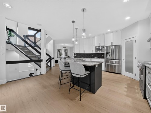 Bright kitchen featuring wood-finish flooring, a central island with a granite-style countertop, stainless steel appliances, white cabinetry, and recessed lighting - #59 10550 Ellerslie Rd Sw, Edmonton, AB - Indoor Photo Showing Kitchen With Upgraded Kitchen