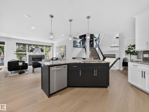 Central kitchen island with a granite countertop, undermount sink, and stainless steel dishwasher - #59 10550 Ellerslie Rd Sw, Edmonton, AB - Indoor Photo Showing Kitchen With Upgraded Kitchen