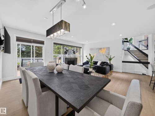 Open-concept living space featuring wood-finish flooring, a contemporary fireplace, and a striking staircase with dark railings - #59 10550 Ellerslie Rd Sw, Edmonton, AB - Indoor Photo Showing Dining Room
