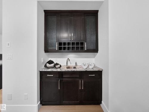Built-in wet bar featuring dark wood cabinetry, a stone-finish countertop, stainless steel sink, and integrated wine rack - #59 10550 Ellerslie Rd Sw, Edmonton, AB - Indoor Photo Showing Other Room