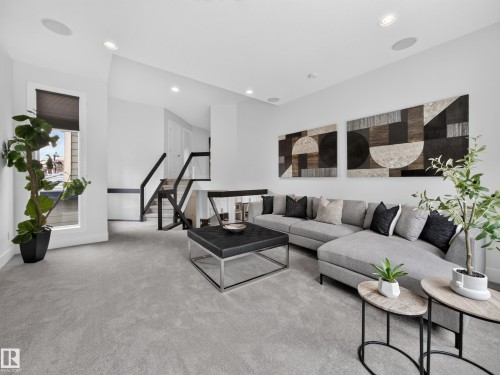 Spacious living area featuring light gray carpeting, recessed lighting, and a contemporary open-tread staircase with black railings - #59 10550 Ellerslie Rd Sw, Edmonton, AB - Indoor Photo Showing Living Room