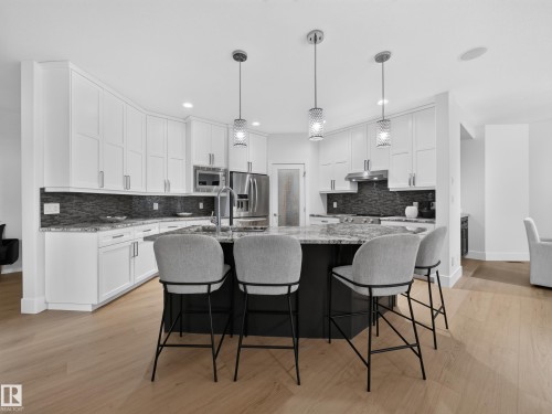Modern kitchen featuring white shaker-style cabinetry, granite countertops, a dark mosaic tile backsplash, and light wood-finish flooring - #59 10550 Ellerslie Rd Sw, Edmonton, AB - Indoor Photo Showing Kitchen With Upgraded Kitchen
