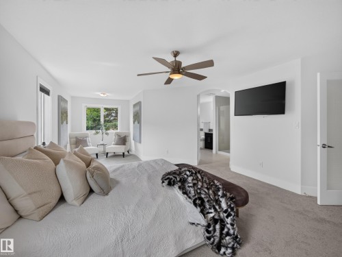 Carpeted room featuring a ceiling fan with integrated lighting, a large window, and an arched doorway opening to an additional space - #59 10550 Ellerslie Rd Sw, Edmonton, AB - Indoor