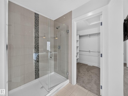 Glass-enclosed shower featuring large format wall tiles with a decorative mosaic accent strip - #59 10550 Ellerslie Rd Sw, Edmonton, AB - Indoor Photo Showing Bathroom