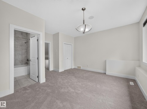 Spacious room featuring plush carpet, a built-in closet with bifold doors, and a contemporary ceiling light fixture - #59 10550 Ellerslie Rd Sw, Edmonton, AB - Indoor