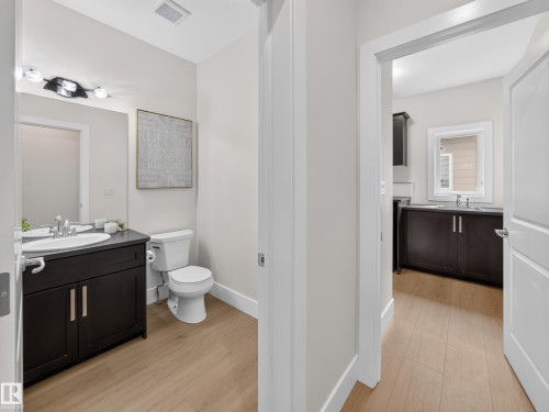 Bathroom featuring a dark wood-finish vanity with a white oval sink, chrome faucet, wall-mounted mirror, and overhead vanity lighting - #59 10550 Ellerslie Rd Sw, Edmonton, AB - Indoor Photo Showing Bathroom