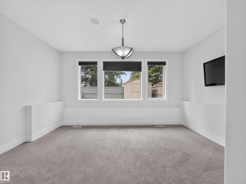 Carpeted room with three large windows, a central ceiling fixture, and a built-in wall-mounted television - #59 10550 Ellerslie Rd Sw, Edmonton, AB - Indoor Photo Showing Other Room