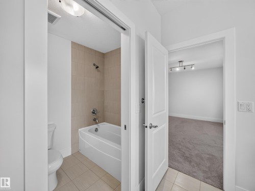 Full bathroom featuring a white tub, shower with tan-toned tile surround, and coordinating floor tiles - #59 10550 Ellerslie Rd Sw, Edmonton, AB - Indoor Photo Showing Bathroom
