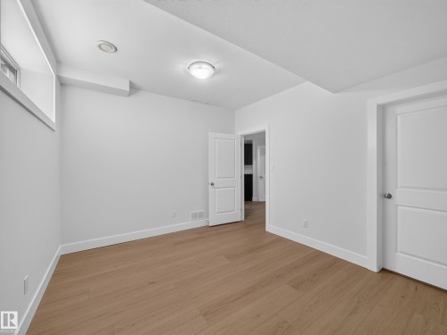 Bright room featuring wood-finish flooring, white walls, two panel doors, an overhead flush mount light, and a window providing natural light - #59 10550 Ellerslie Rd Sw, Edmonton, AB - Indoor Photo Showing Other Room