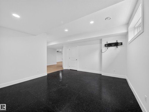 Spacious open-concept room featuring durable black speckled flooring, recessed lighting, white baseboards, and a wall-mounted bracket - #59 10550 Ellerslie Rd Sw, Edmonton, AB - Indoor Photo Showing Other Room