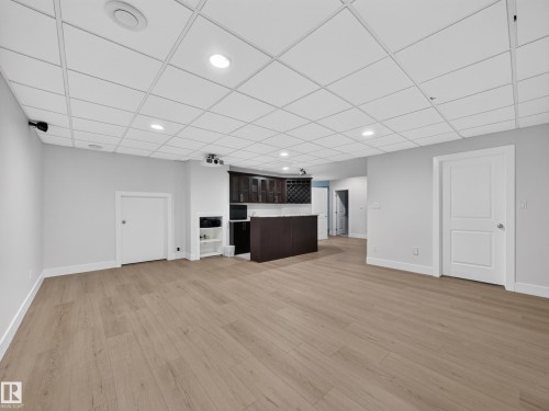 Spacious open room featuring wood-finish flooring, recessed lighting, and a built-in wet bar with dark cabinetry and a wine rack - #59 10550 Ellerslie Rd Sw, Edmonton, AB - Indoor