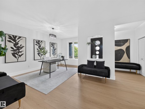 Spacious room featuring wood-finish flooring, white walls, and a contemporary chandelier - #59 10550 Ellerslie Rd Sw, Edmonton, AB - Indoor