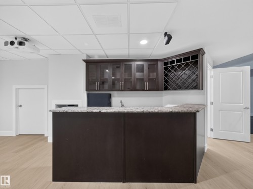 Wet bar featuring a light-toned countertop, dark wood-finish cabinetry, a built-in wine rack, and a sink with a faucet - #59 10550 Ellerslie Rd Sw, Edmonton, AB - Indoor