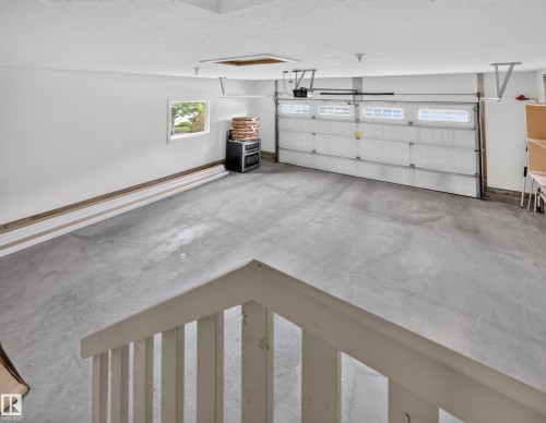 Spacious garage featuring a concrete floor, overhead lighting, and a white paneled garage door with upper window inserts - #59 10550 Ellerslie Rd Sw, Edmonton, AB - Indoor Photo Showing Garage