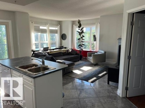 Kitchen island with integrated double basin sink, white cabinetry, and dark countertop - #407 11103 84 Av Nw, Edmonton, AB 