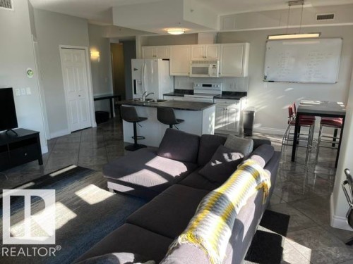 Open-concept living area with tile flooring, featuring a kitchen with white cabinetry and a breakfast bar - #407 11103 84 Av Nw, Edmonton, AB 