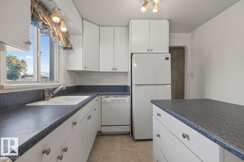 White cabinetry, dark countertops, built-in sink, white refrigerator, and a built-in dishwasher - 12309 128 Street Nw, Edmonton, AB 