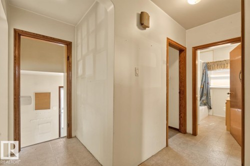 Hallway featuring neutral wall finishes, tile flooring, and wood-finish door frames - 12309 128 Street Nw, Edmonton, AB 