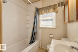 White tiled tub/shower combination with integrated corner shelving, single hung window with blinds, wall-mounted medicine cabinet with wood trim, and a white vanity with an integrated sink - 