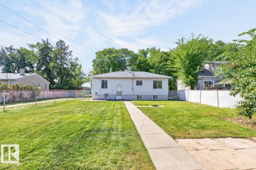 Expansive backyard featuring a manicured lawn, concrete pathway, and mature trees, enclosed by a chain link fence and a privacy fence - 12309 128 Street Nw, Edmonton, AB 